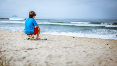 The boy sat down on the ball gazing at the sea
